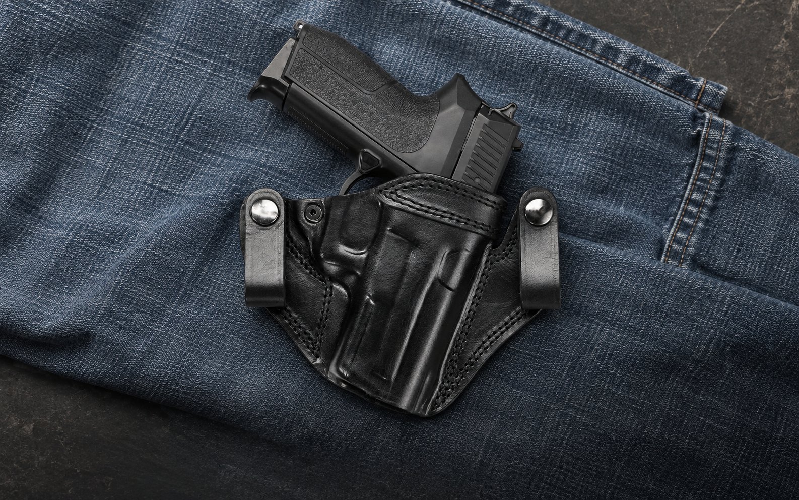 Funda IWB de cuero negro con dos presillas a presión sobre mezclilla azul